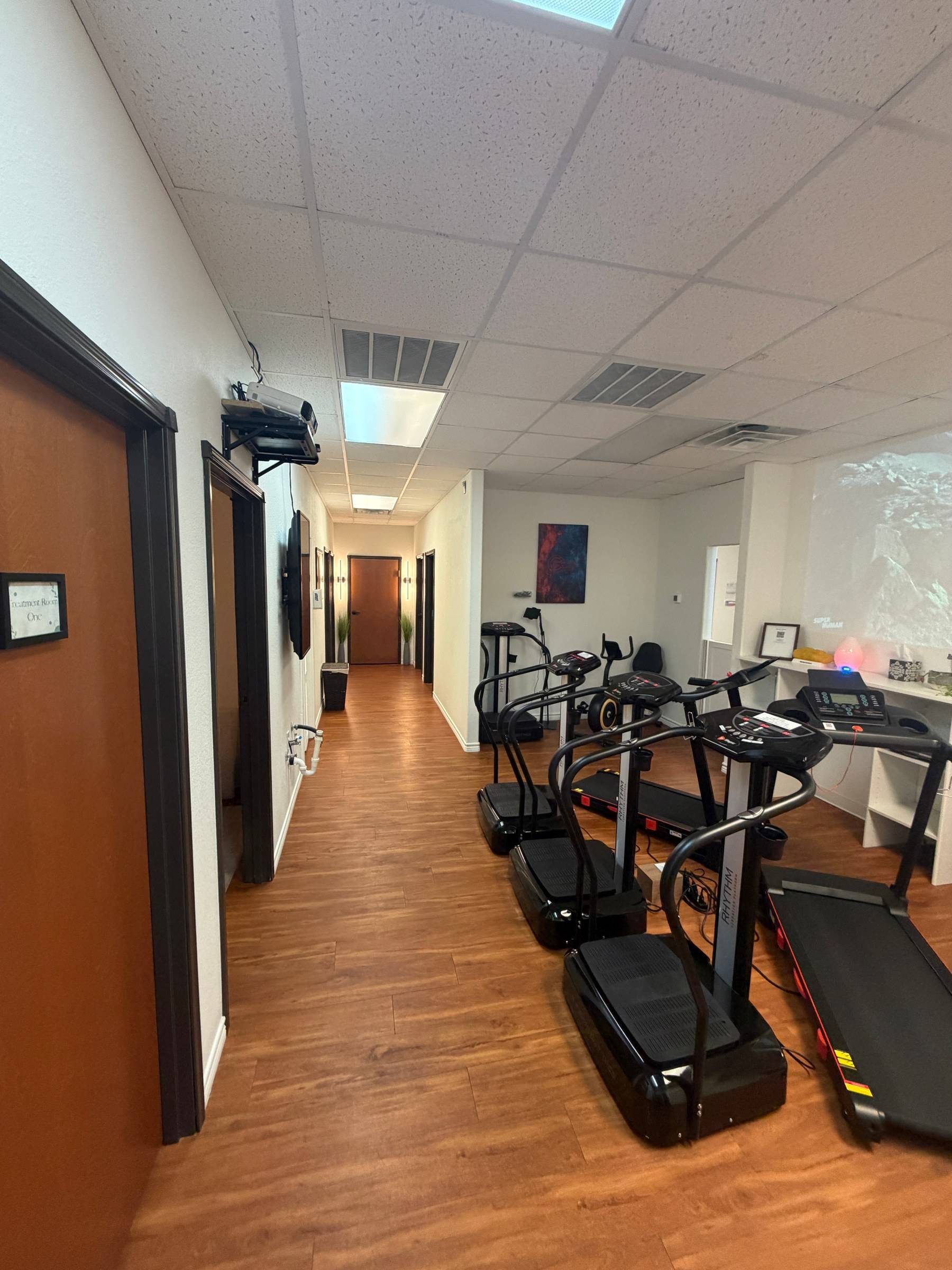 The cardio bay hallway at Genesis Red Light: vibration plates and treadmills on a wood floor