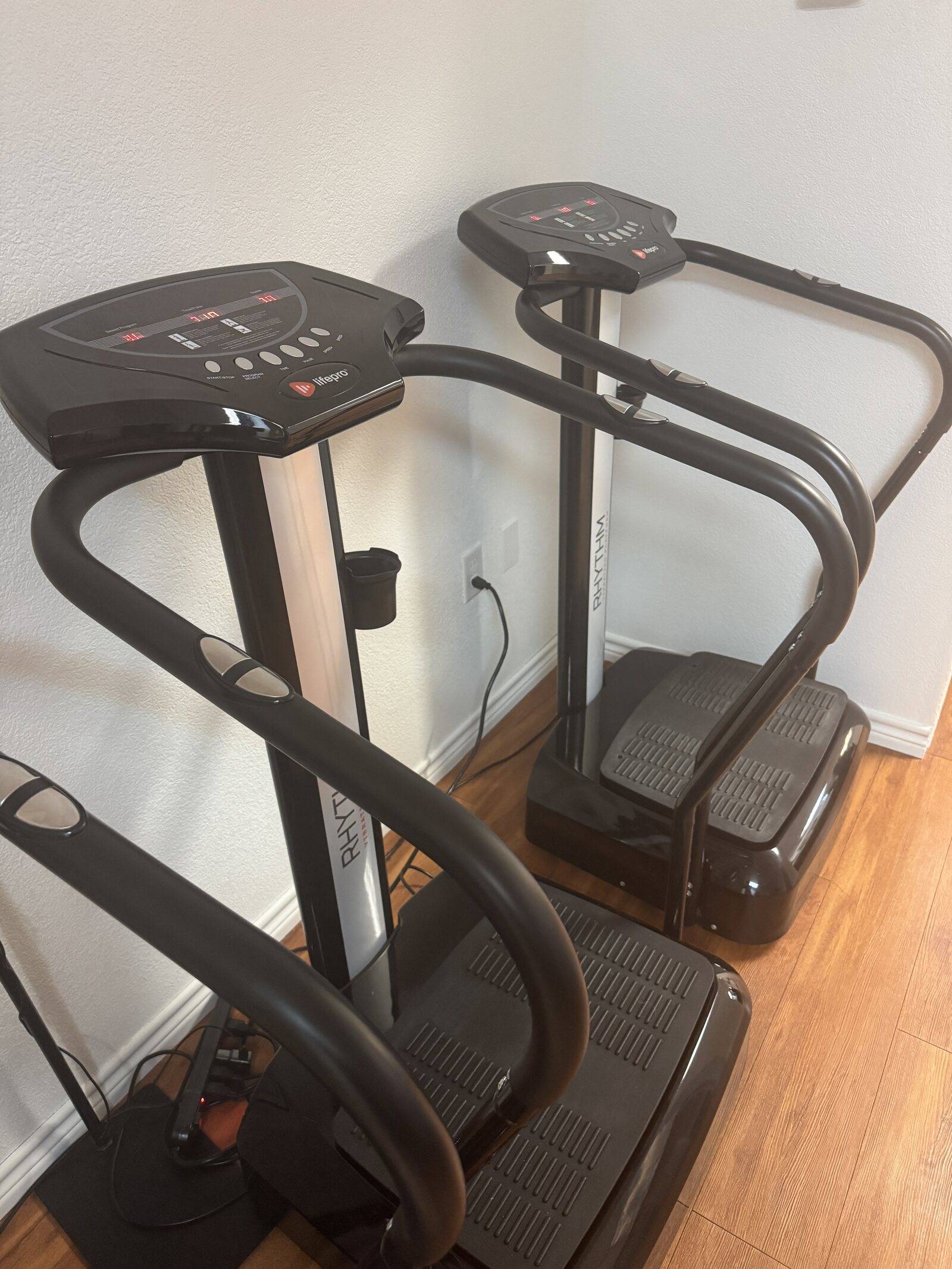 Two vibration plates with handlebars on the wood floor at Genesis Red Light, Cedar Park
