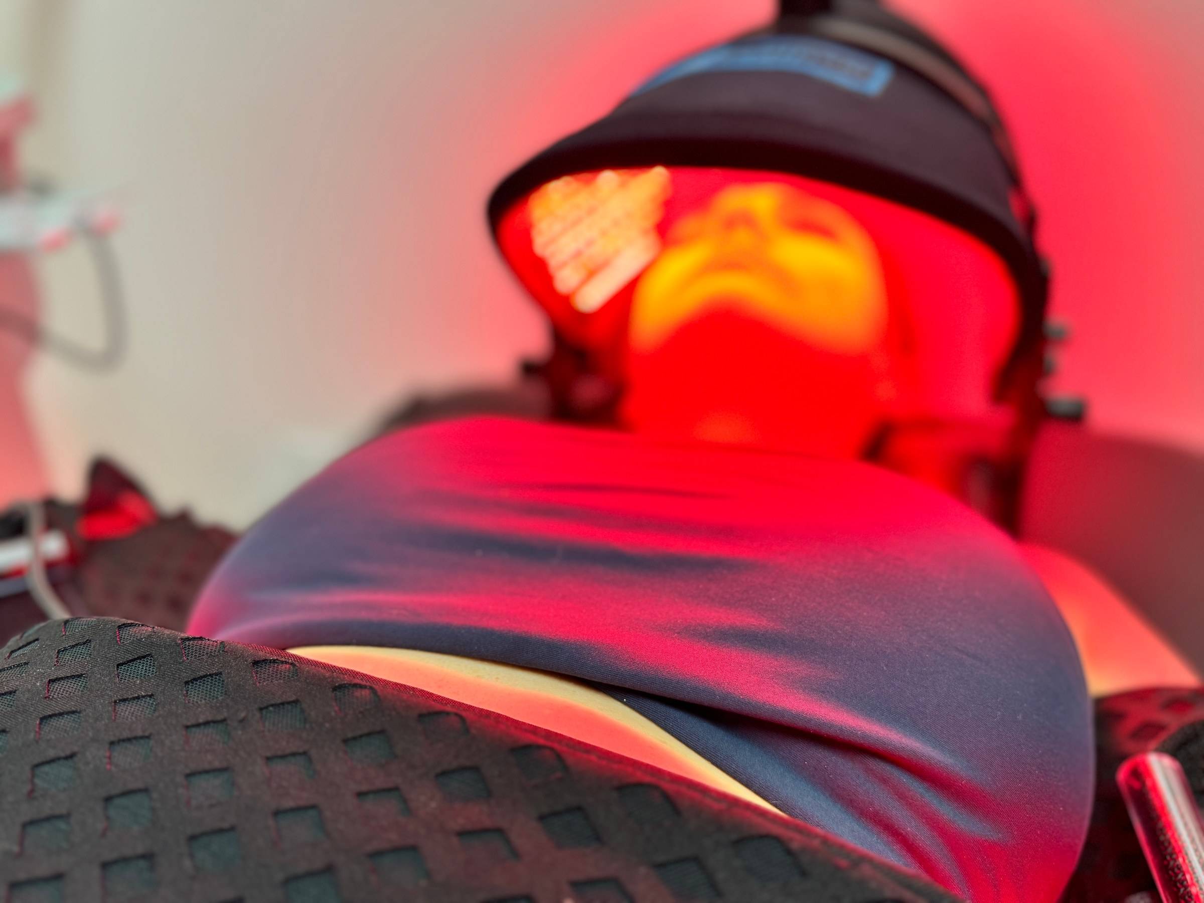 A client resting with eyes closed under the Contour Light red LED face panel, pads around the waist, at Genesis Red Light