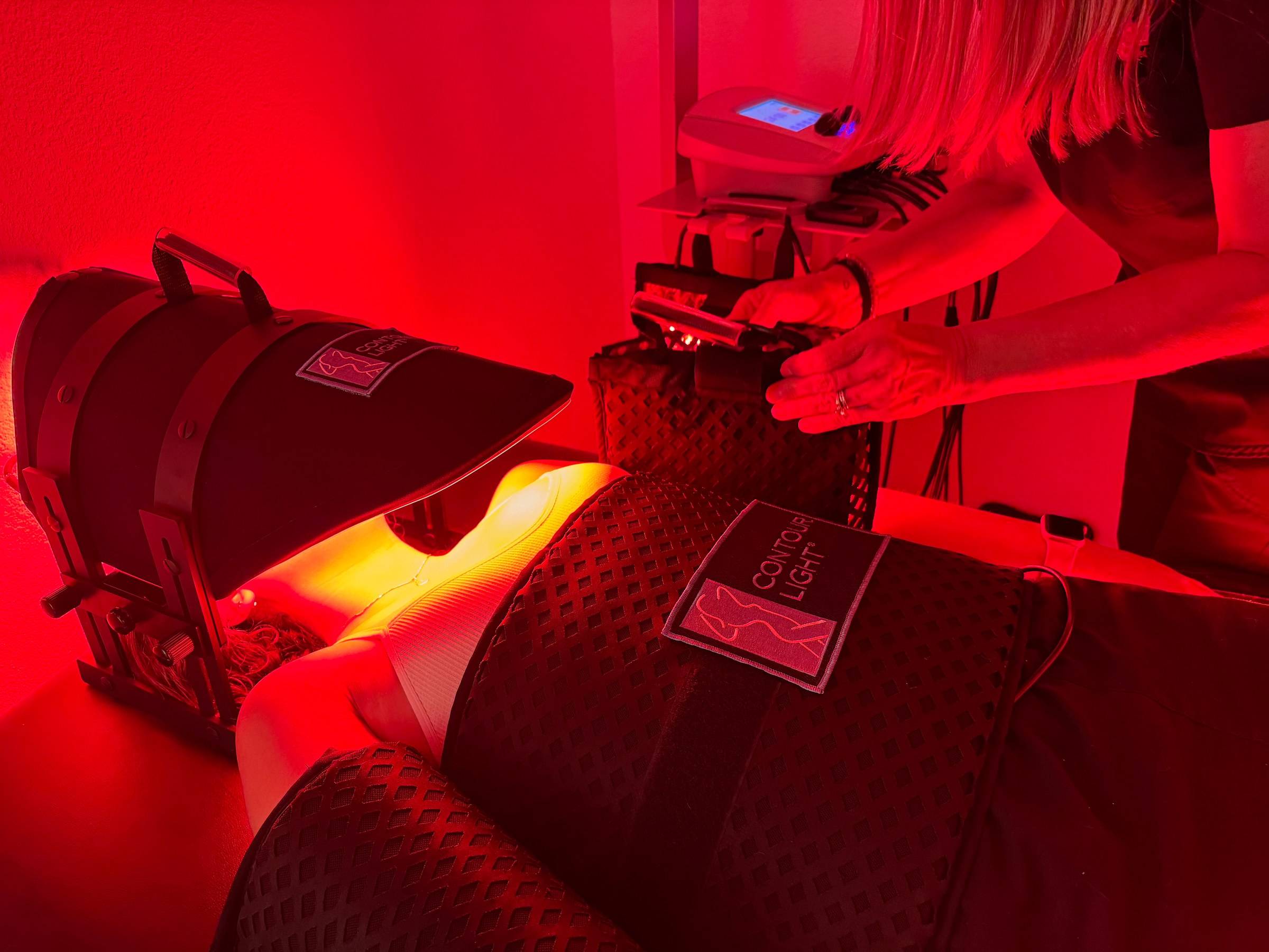 A Genesis Red Light team member adjusts the Contour Light pads on a client lying under the red LED face light in a private room in Cedar Park, TX