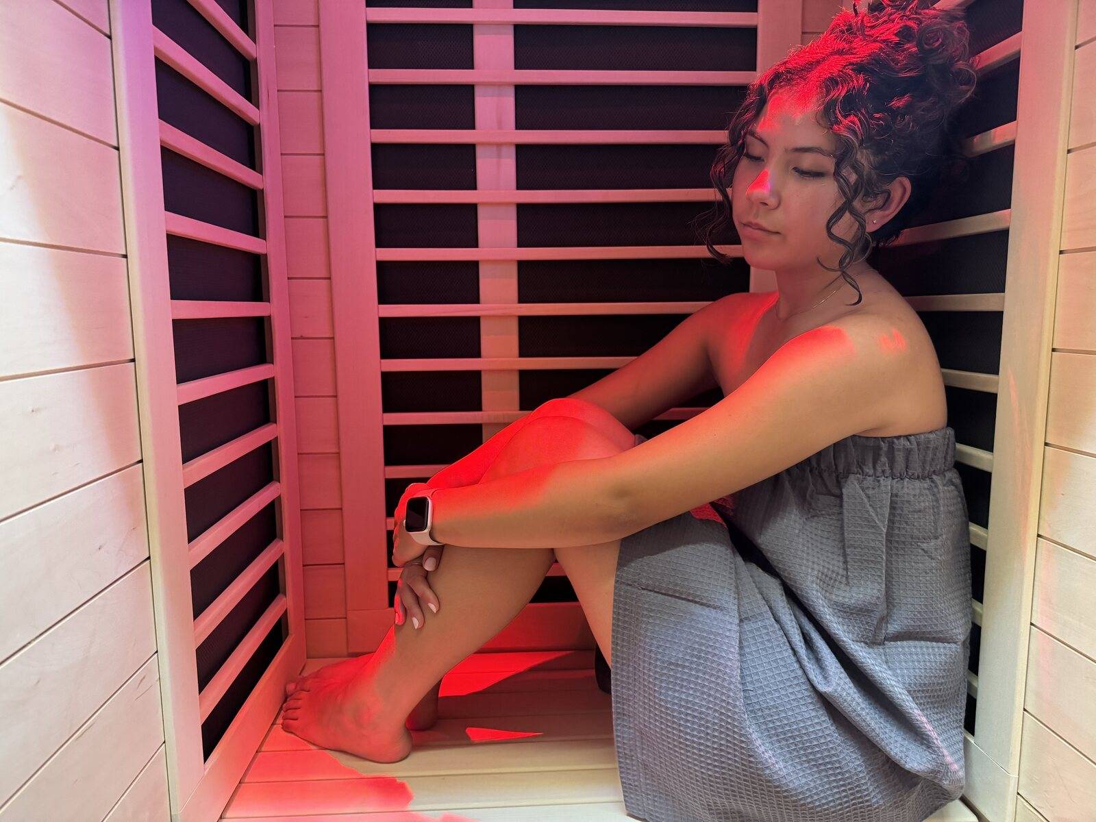 A woman wrapped in a towel resting in the private infrared sauna at Genesis Red Light in Cedar Park